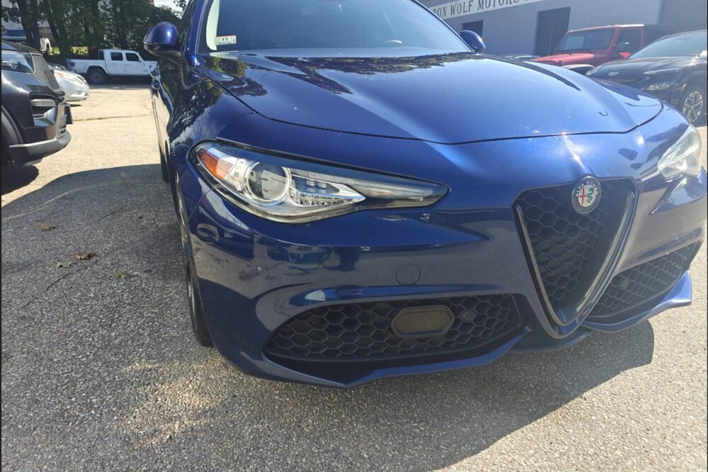 Blue Alfa Romeo Giulia parked outside Iron Wolf Motors in Worcester, MA, with the shop sign behind it