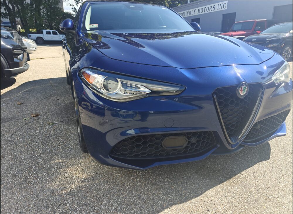 The repaired dark blue Alfa Romeo Giulia with a clear, correctly aligned headlamp and straight bumper, parked outside Iron Wolf Motors in Worcester, MA
