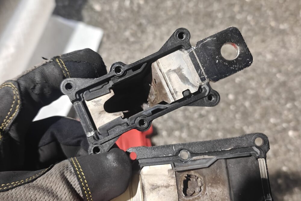 A high-voltage pyrofuse removed from a Tesla, held in a gloved hand, at Iron Wolf Motors in Worcester, MA