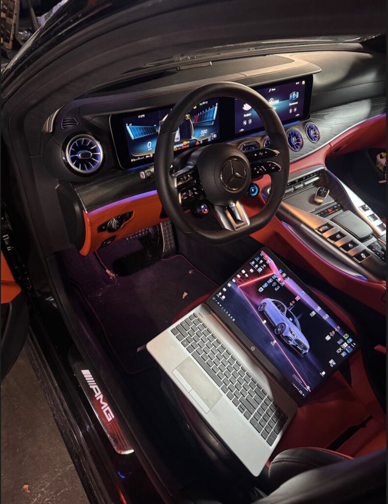 Service laptop running ECU module coding in the footwell of a Mercedes-AMG at Iron Wolf Motors in Worcester, MA