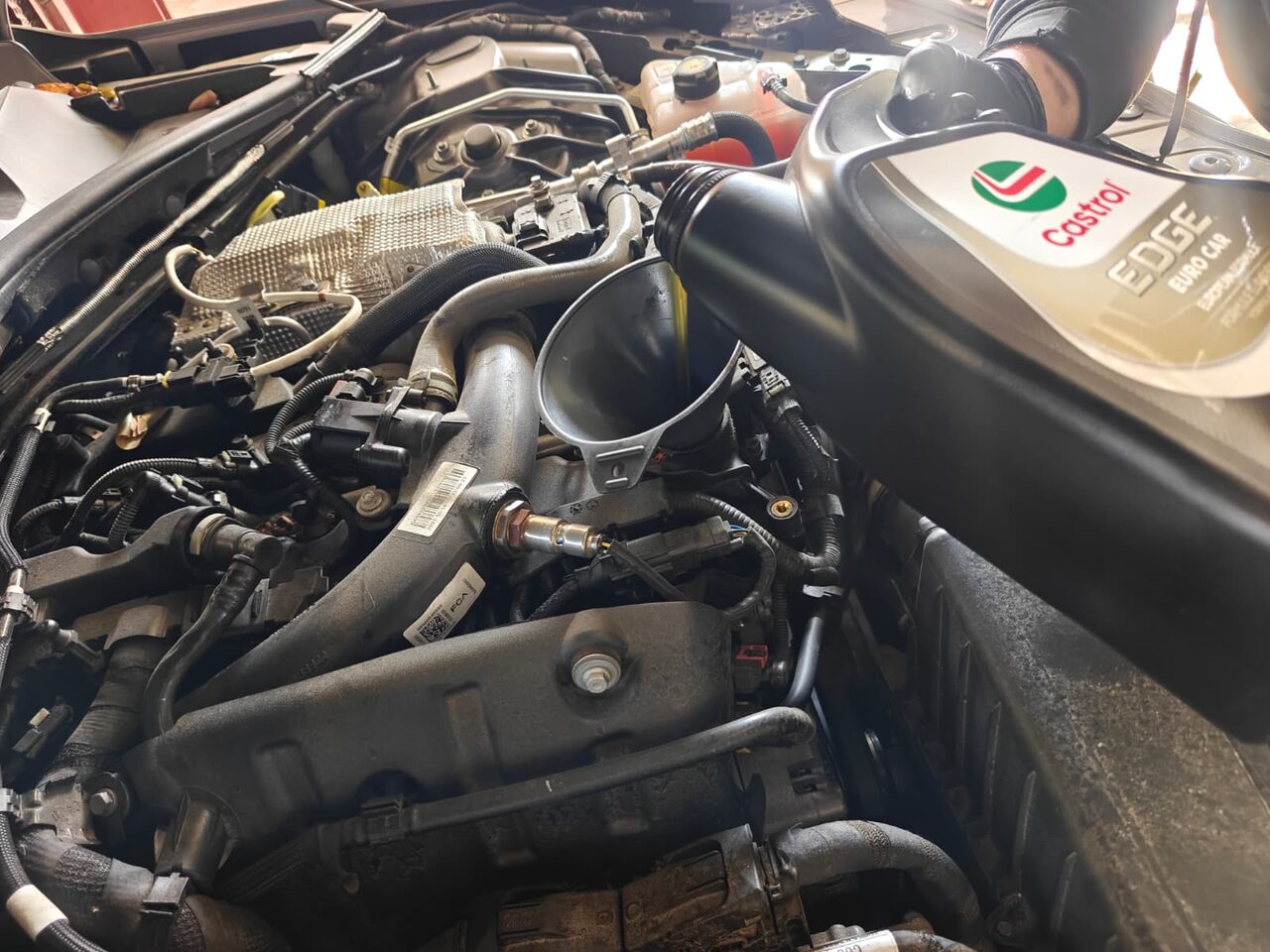 Technician pouring Castrol EDGE Euro Car full-synthetic oil through a funnel into the engine of an Alfa Romeo Giulia 2.0 turbo
