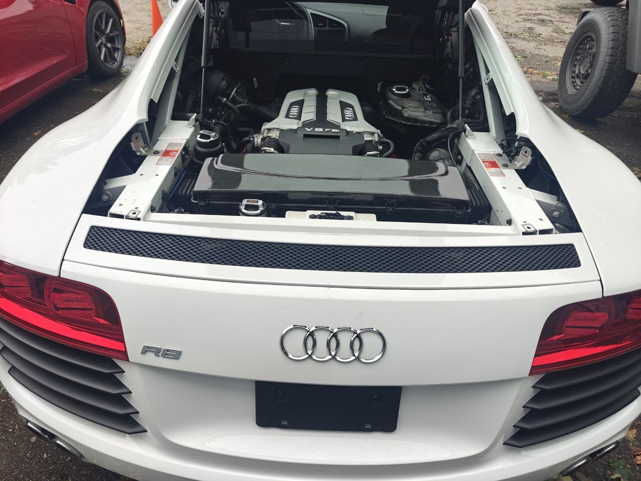 Rear engine bay of a white Audi R8 with the engine cover open, showing the 4.2 V8 FSI intake manifold and carbon fibre cover