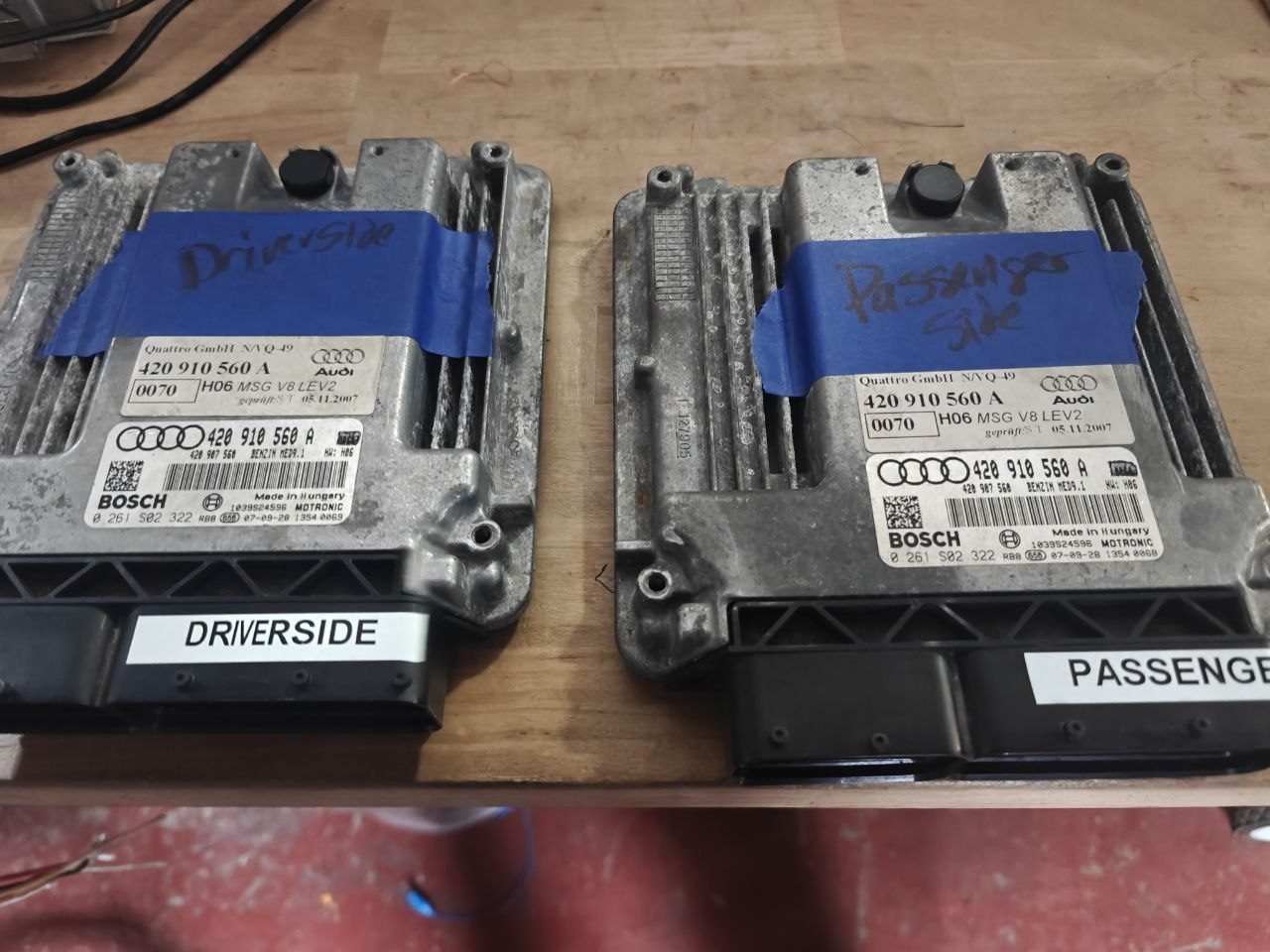 Two Bosch ME9.1 engine control units from an Audi R8 4.2 V8 on the workbench, both labelled 420 910 560 A, marked with blue tape and labels as driver side and passenger side