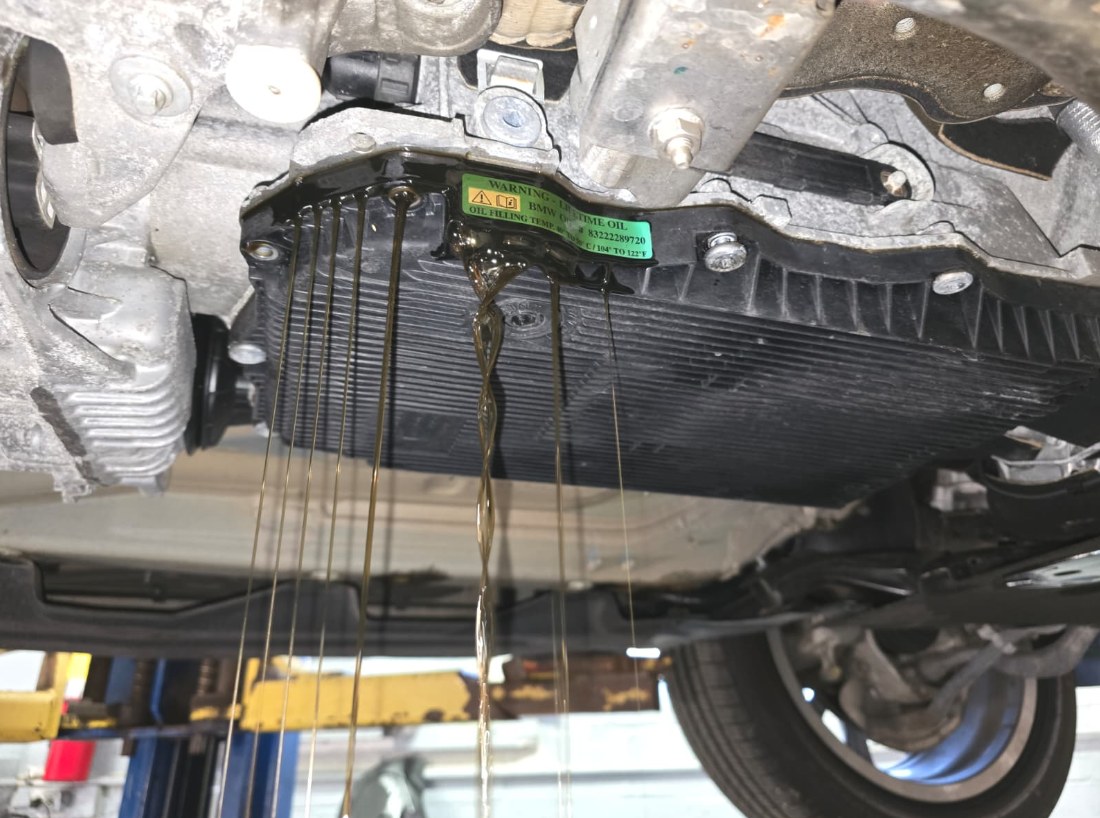 Transmission fluid streaming off the edges of a BMW X3 ZF 8-speed pan, with the green Lifetime oil sticker visible on the pan