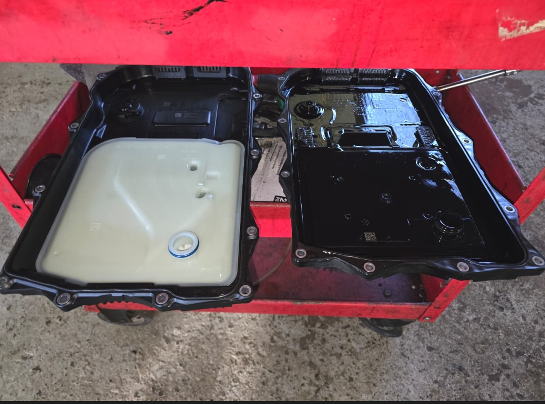 New transmission pan with integrated filter next to the old oil-coated pan from a BMW X3, on a red shop cart
