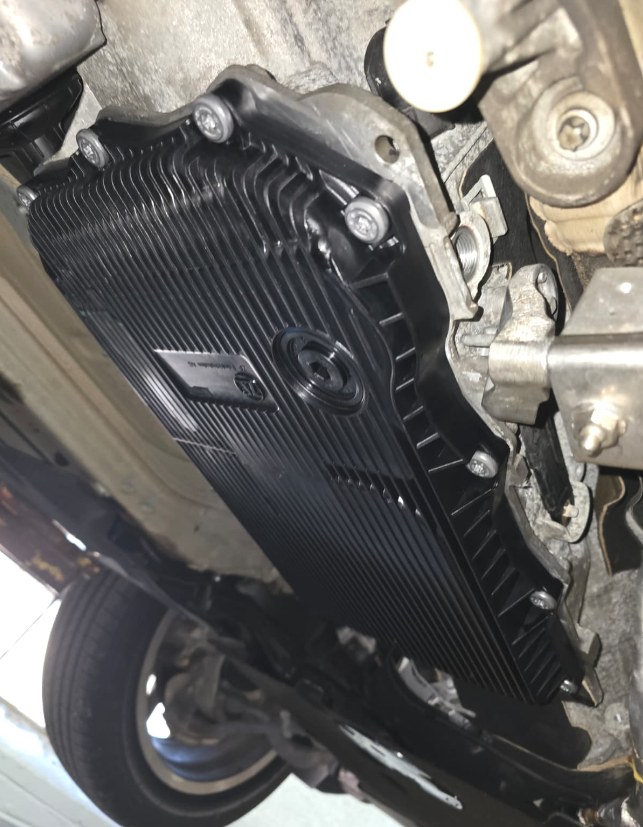 Side view of the new transmission pan installed on a BMW X3, with the fill plug area visible