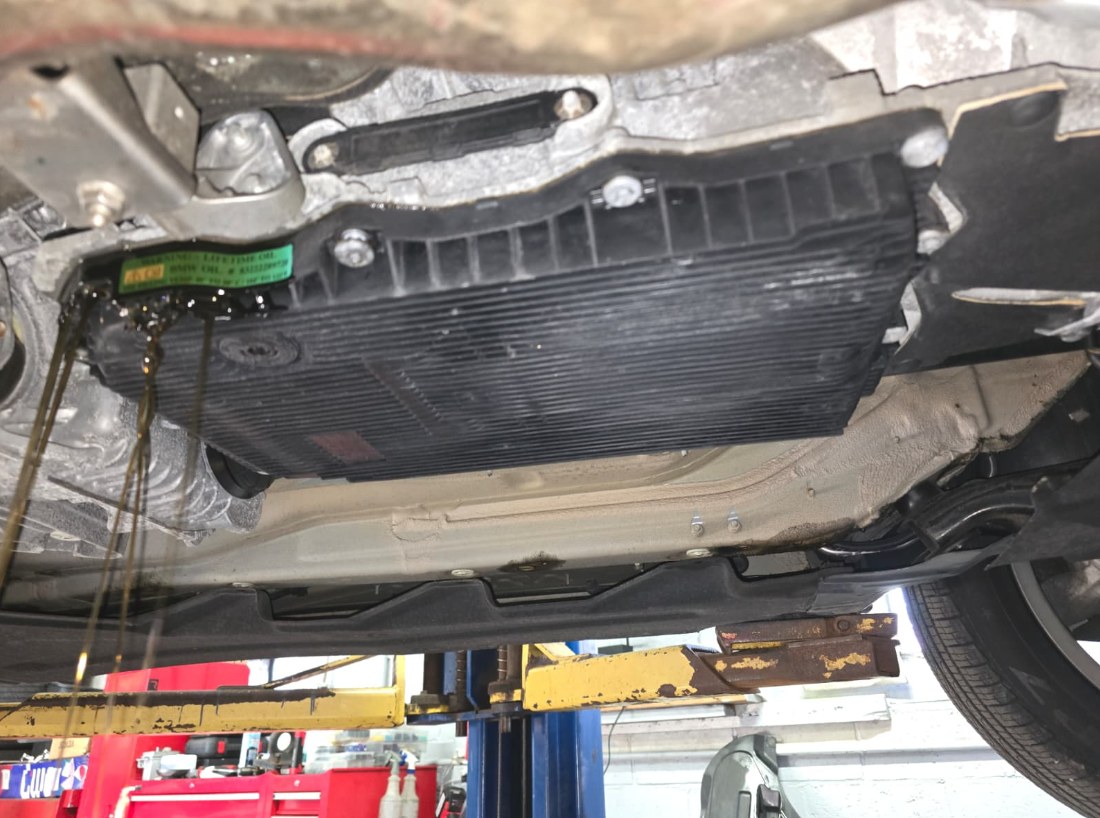 Wider view under a 2021 BMW X3 on a lift with transmission fluid draining off the pan