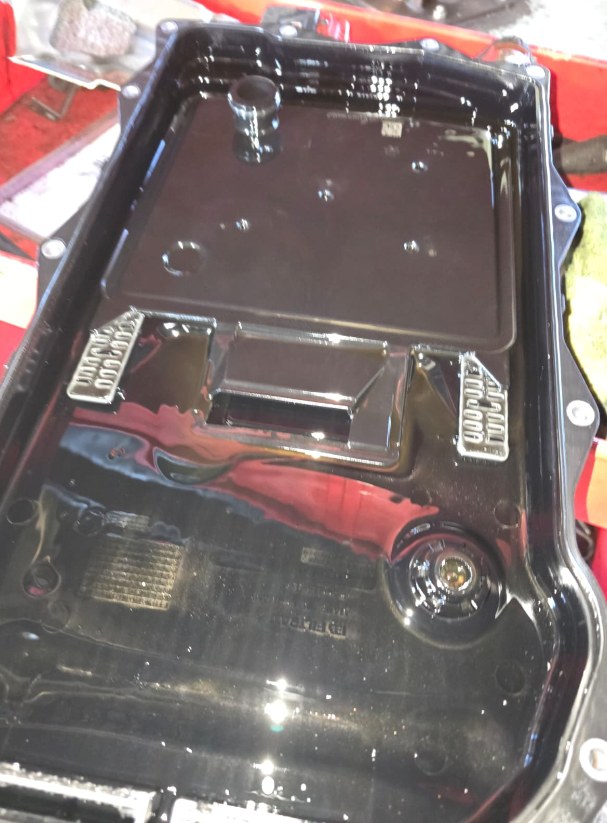Inside of the old transmission pan from a BMW X3, coated in old fluid, with the magnets visible