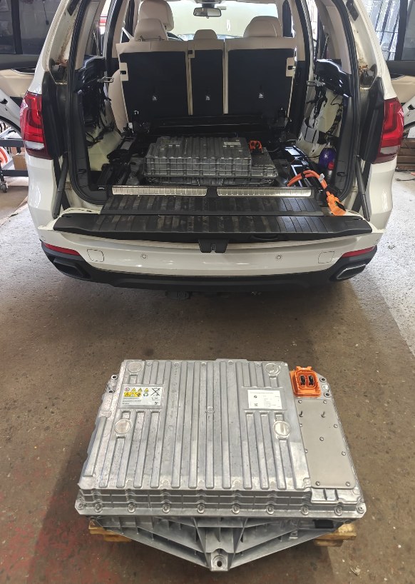High-voltage battery pack from a 2016 BMW X5 xDrive40e on a pallet on the shop floor behind the open cargo area of the white SUV