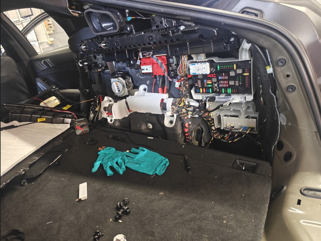Side of the BMW X6 cargo area with the trim panel removed, showing the rear fuse box and wiring harnesses