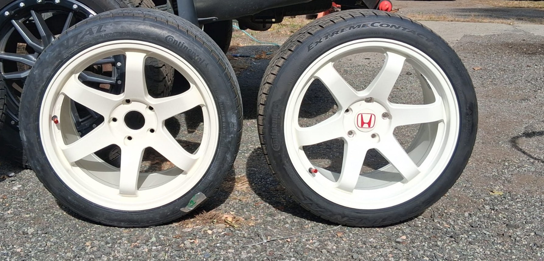 Two white six-spoke Honda Civic Type R wheels with Continental tires side by side: the refinished wheel on the left and the original on the right with its red H center cap