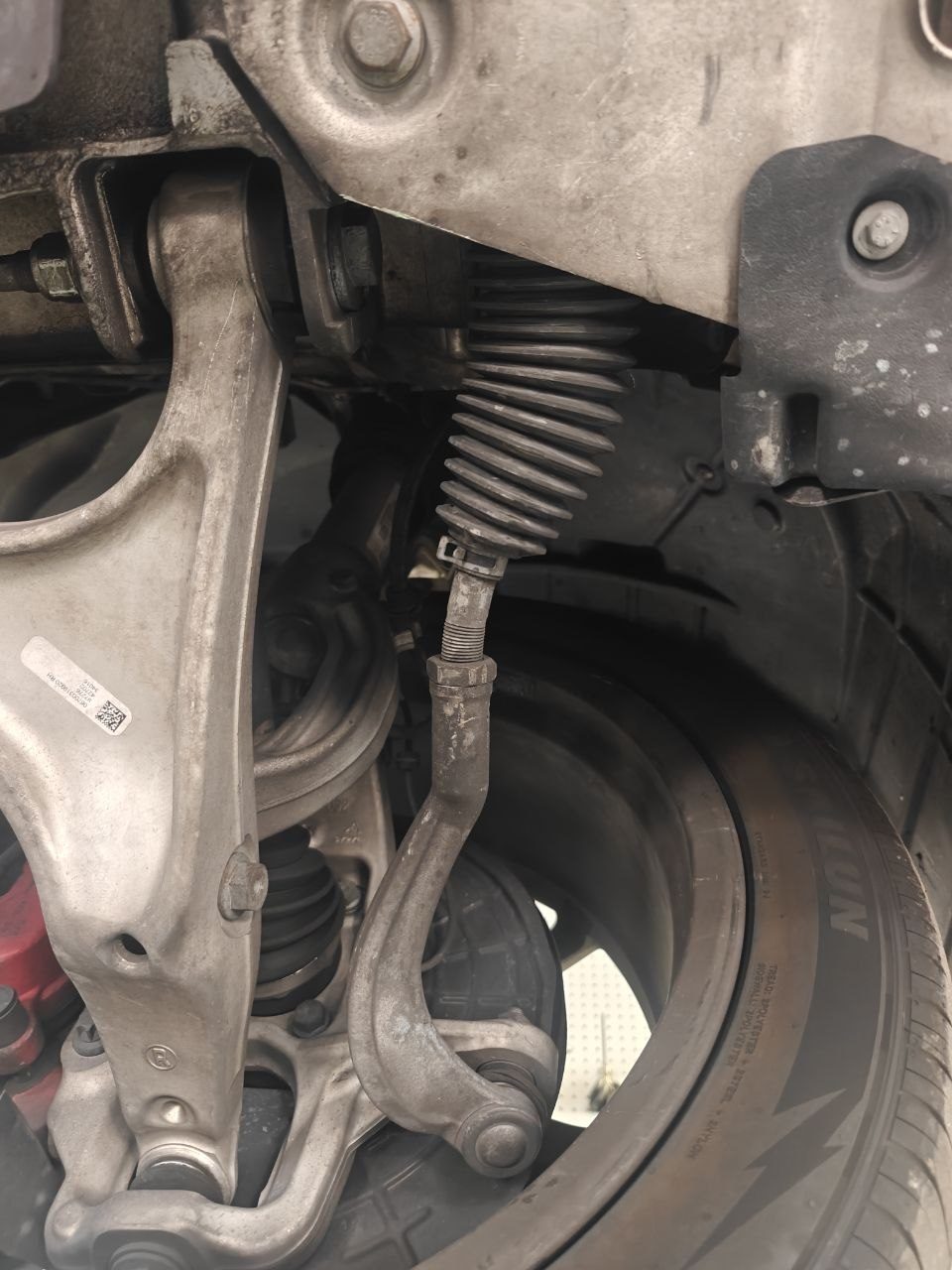Underside view of the front steering on a 2017 Maserati Levante showing the outer tie rod running from the steering rack boot to the steering knuckle with a visible S-shaped bend along its length