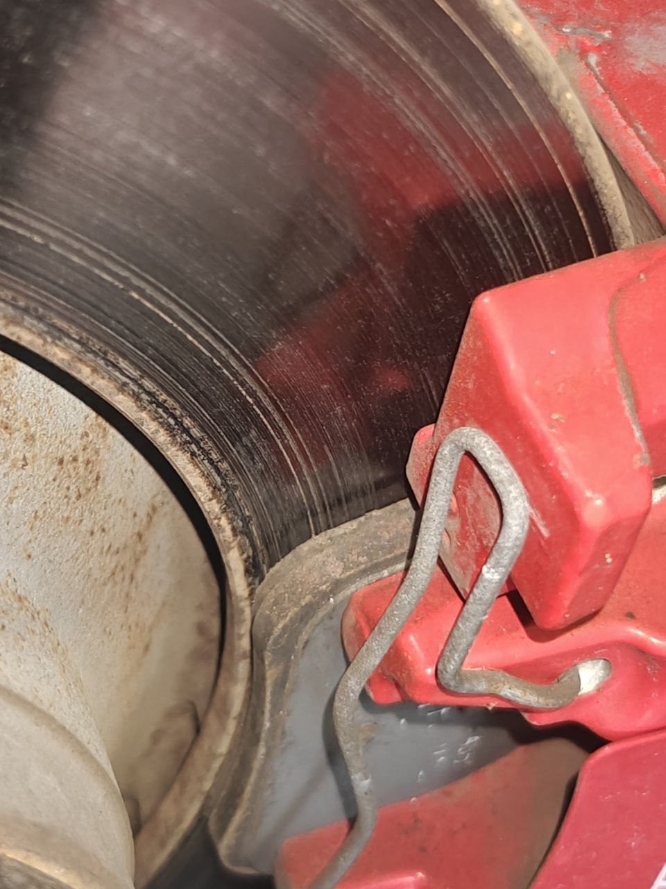 Red brake caliper and pad retaining spring on a 2017 Maserati Levante next to a worn front rotor with heavy grooving across its face and a ridge at the inner edge of the braking surface