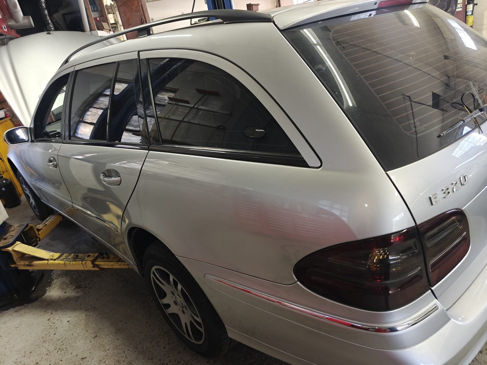 Silver Mercedes-Benz E320 wagon on a lift in the Iron Wolf Motors shop with the hood open