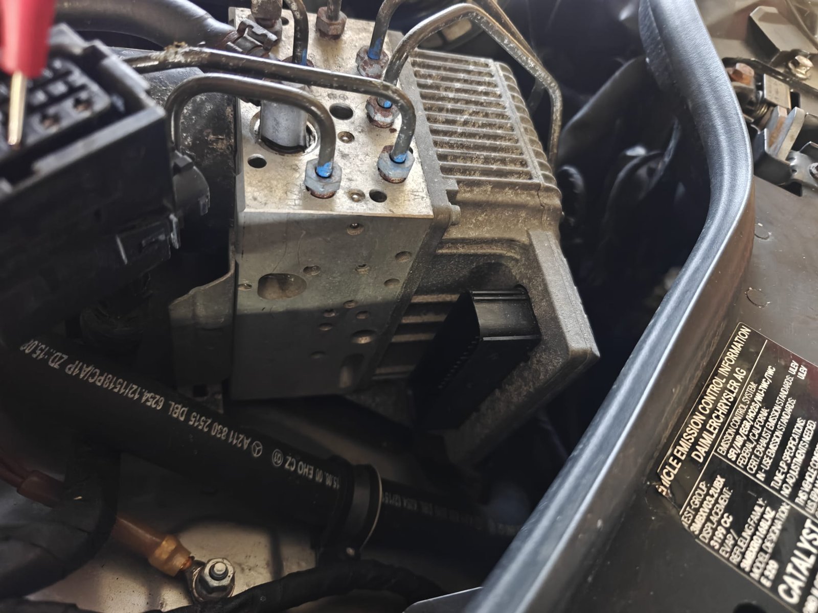 The SBC brake unit of a Mercedes E320 with its brake lines and electronic module, a test lead back-probing its connector