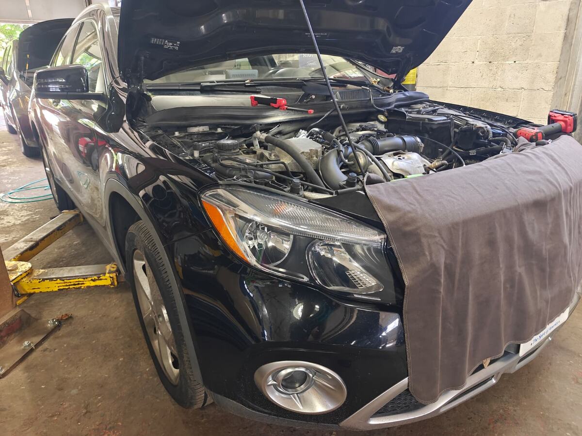 Mercedes-Benz GLA250 pulled into a service bay at Iron Wolf Motors with the hood raised, a fender cover over the front end and the lift arms positioned under the car