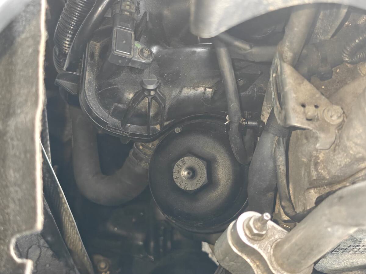 Close-up of the oil filter housing cap on the M270 engine of a Mercedes-Benz GLA250, fitted to the engine and surrounded by coolant hoses and wiring, with oil residue across the area