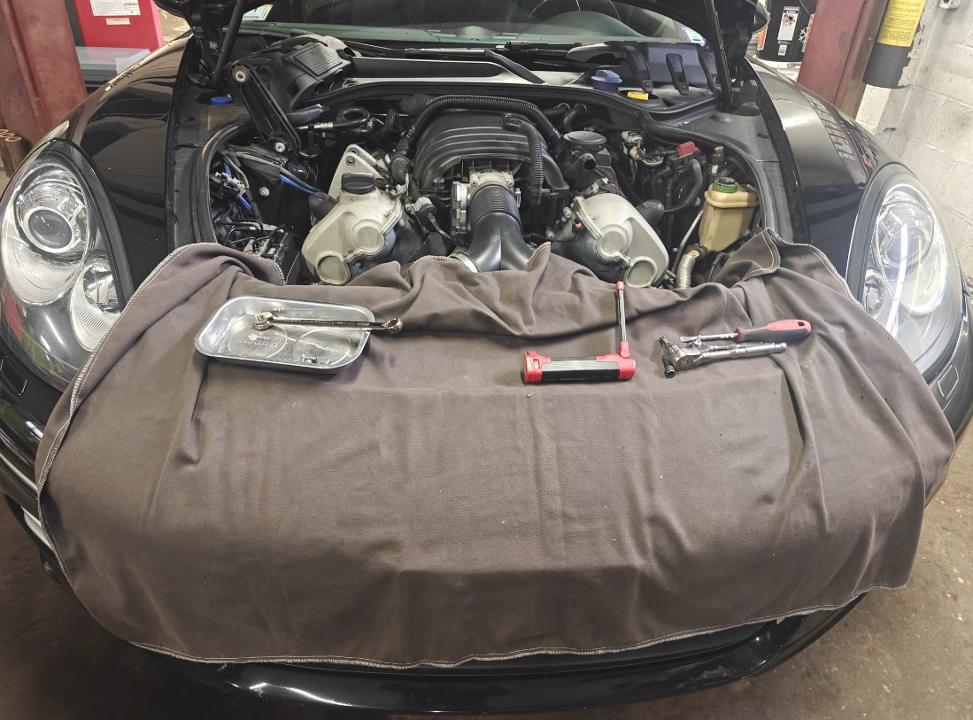 Porsche Panamera engine bay with a fender cover over the front and tools laid out for the thermostat replacement